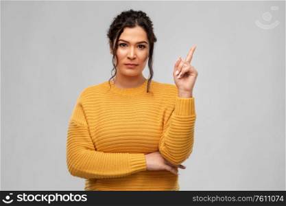 people concept - serious young woman with pierced nose pointing finger up over grey background. serious young woman pointing finger up