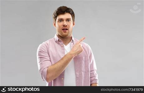 people concept - shocked young man showing something over grey background. shocked young man showing something