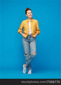 people concept - smiling red haired teenage girl in checkered shirt and torn jeans over bright blue background. red haired teenage girl in shirt and torn jeans