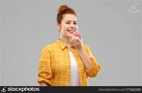 people concept - smiling red haired teenage girl in checkered shirt eating donut with pink icing over grey background. smiling red haired teenage girl eating donut
