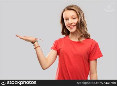 people concept - smiling teenage girl with long hair in red t-shirt holding something imaginary on empty hand over grey background. smiling teenage girl holding empty hand
