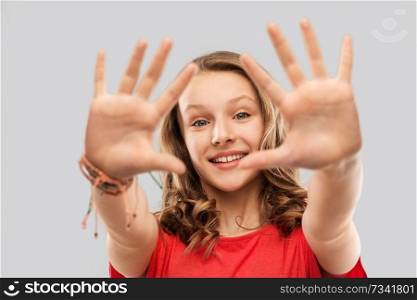 people concept - smiling teenage girl with long hair in red t-shirt giving high five over grey background. happy teenage girl in red t-shirt giving high five
