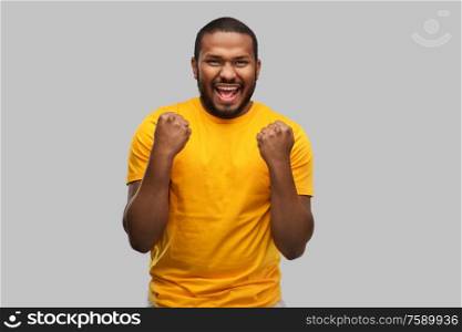people concept - smiling young african american man in yellow t-shirt celebrating success over grey background. smiling african american man celebrating success