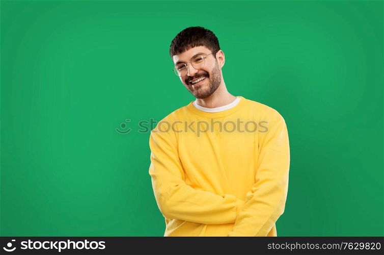 people concept - smiling young man in glasses and yellow sweatshirt over emerald green background. smiling young man in glasses and yellow sweatshirt