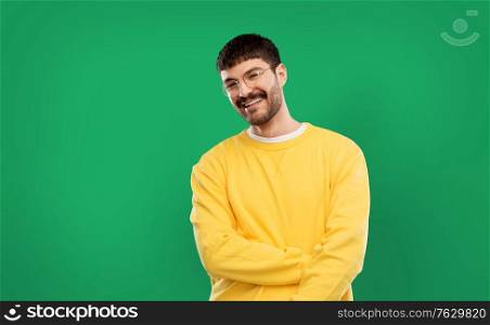 people concept - smiling young man in glasses and yellow sweatshirt over emerald green background. smiling young man in glasses and yellow sweatshirt
