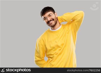 people concept - smiling young man in glasses and yellow sweatshirt over grey background. smiling young man in glasses and yellow sweatshirt