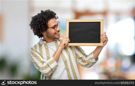 people concept - smiling young man in glasses holding chalkboard over office background. smiling man with chalkboard at office