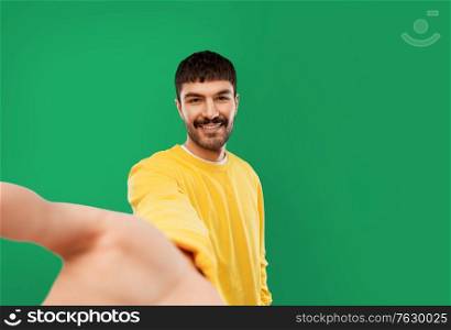 people concept - smiling young man in yellow sweatshirt making selfie over emerald green background. happy young man in yellow sweatshirt making selfie