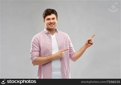 people concept - smiling young man showing something over grey background. smiling young man showing something