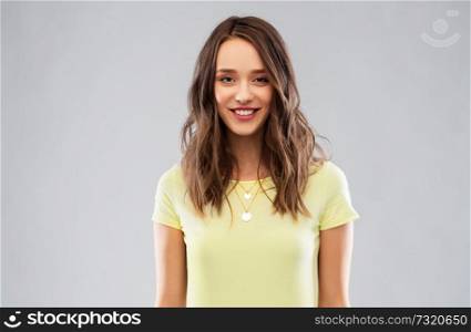 people concept - smiling young woman or teenage girl in blank yellow t-shirt over grey background. young woman or teenage girl in yellow t-shirt