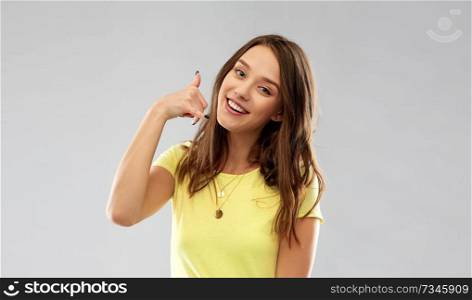 people concept - smiling young woman or teenage girl in blank yellow t-shirt showing phone call gesture over grey background. young woman or teenage girl showing call gesture