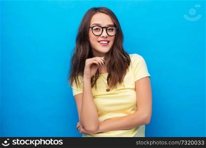 people concept - smiling young woman or teenage girl in yellow t-shirt and glasses over bright blue background. young woman or teenage girl in glasses