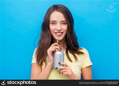 people concept - smiling young woman or teenage girl in yellow t-shirt drinking soda from can through paper straw over bright blue background. young woman or teenage girl drinking soda from can