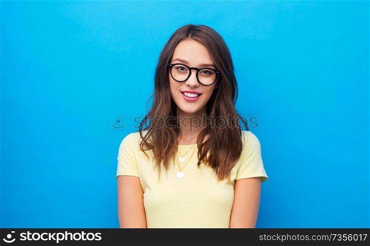 people concept - smiling young woman or teenage girl in yellow t-shirt and glasses over bright blue background. young woman or teenage girl in glasses