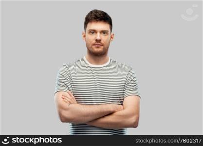 people concept - young man in striped t-shirt with crossed arms over grey background. young man in striped t-shirt with crossed arms
