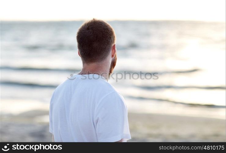 people concept - young man in white t-shirt on beach looking at sea. young man in white t-shirt on beach looking at sea