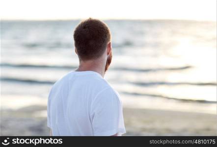 people concept - young man in white t-shirt on beach looking at sea. young man in white t-shirt on beach looking at sea