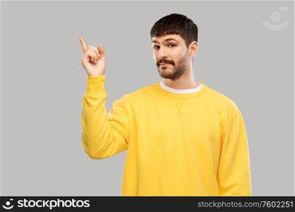 people concept - young man in yellow sweatshirt pointing finger to something over grey background. man pointing finger to something