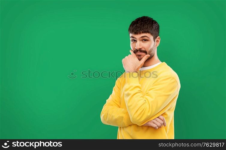 people concept - young man in yellow sweatshirt thinking over emerald green background. thinking young man in yellow sweatshirt