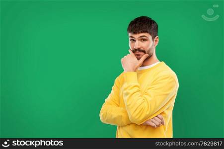 people concept - young man in yellow sweatshirt thinking over emerald green background. thinking young man in yellow sweatshirt