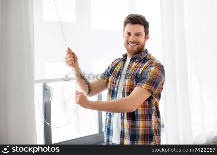 people concept - young man opening or closing roller blind on window at home. man opening roller blind on window at home