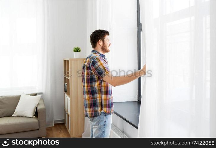 people concept - young man opening window curtain at home. young man opening window curtain at home