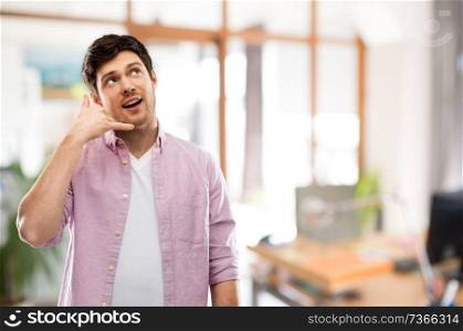 people concept - young man showing phone call gesture over office room background. man showing phone call gesture over office room
