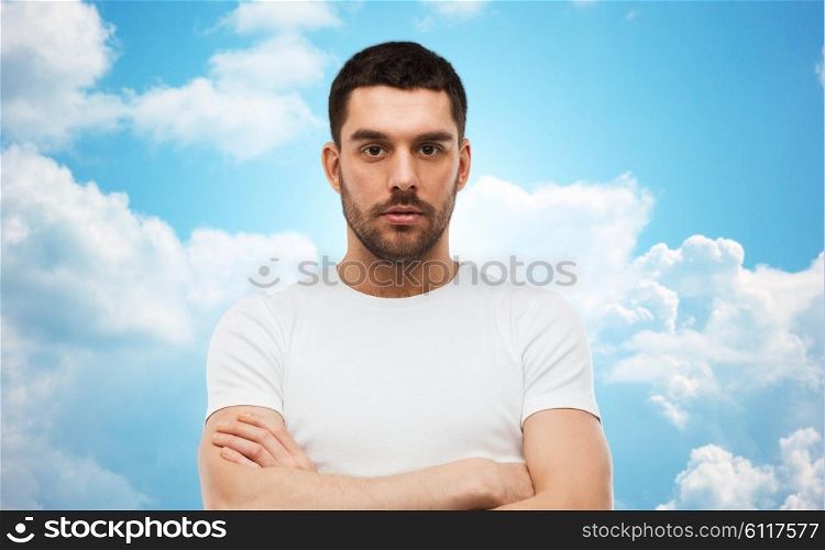 people concept - young man with crossed arms over blue sky and clouds background. young man with crossed arms over blue sky