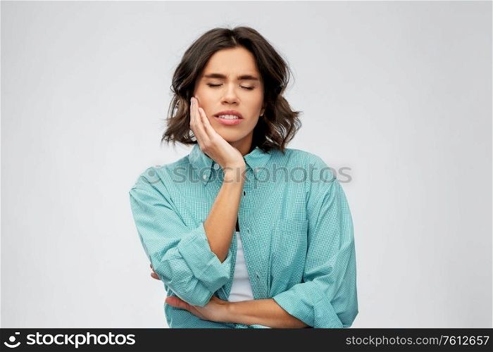 people concept - young woman in turquoise shirt suffering from toothache over grey background. young woman suffering from toothache