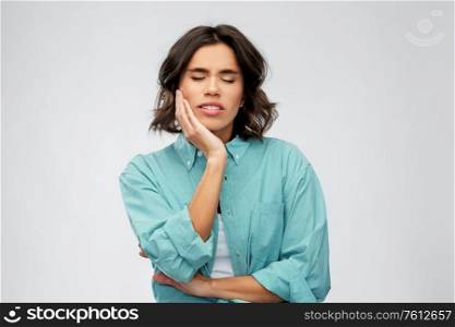 people concept - young woman in turquoise shirt suffering from toothache over grey background. young woman suffering from toothache