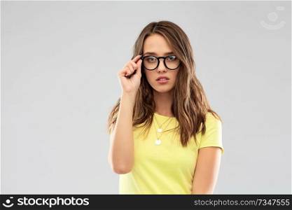 people concept - young woman or teenage girl in yellow t-shirt and glasses over grey background. young woman or teenage girl in glasses
