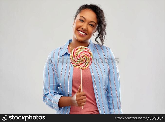 people, confectionery and sweets concept - happy african american young woman with big lollipop over pink background. happy african american woman with big lollipop