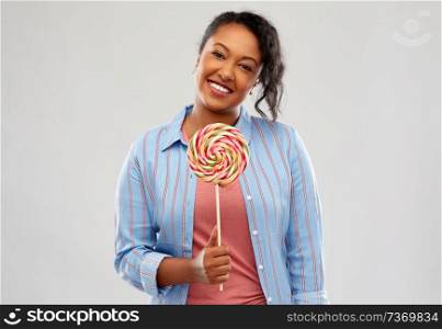 people, confectionery and sweets concept - happy african american young woman with big lollipop over pink background. happy african american woman with big lollipop