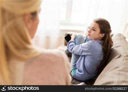 people, conflict and family concept - sad girl with smartphone looking at her mother at home. sad girl with smartphone looking at mother at home