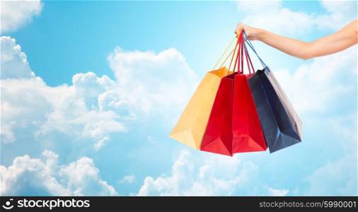 people, consumerism and sale concept - close up of female hand holding shopping bags over blue sky and clouds background