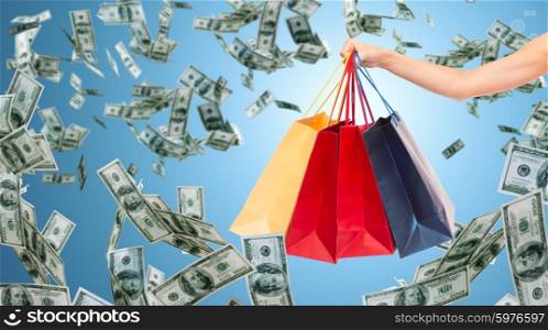 people, consumerism, finance and sale concept - close up of female hand holding shopping bags over blue background and money rain