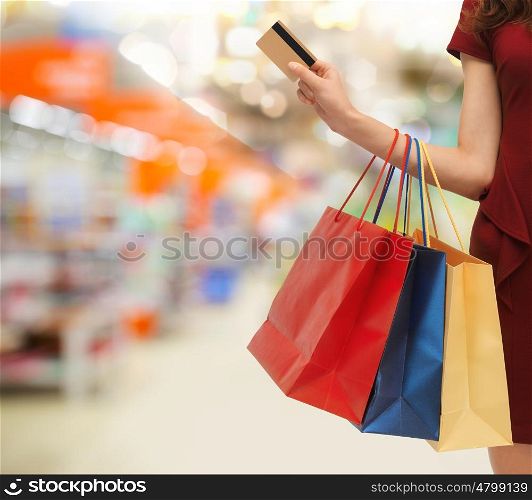 people, consumerism, finances and sale concept - close up of woman with shopping bags and credit card over supermarket background