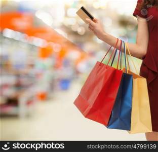 people, consumerism, finances and sale concept - close up of woman with shopping bags and credit card over supermarket background