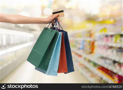 people, consumerism, finances and sale concept - hand with shopping bags and credit card over supermarket background