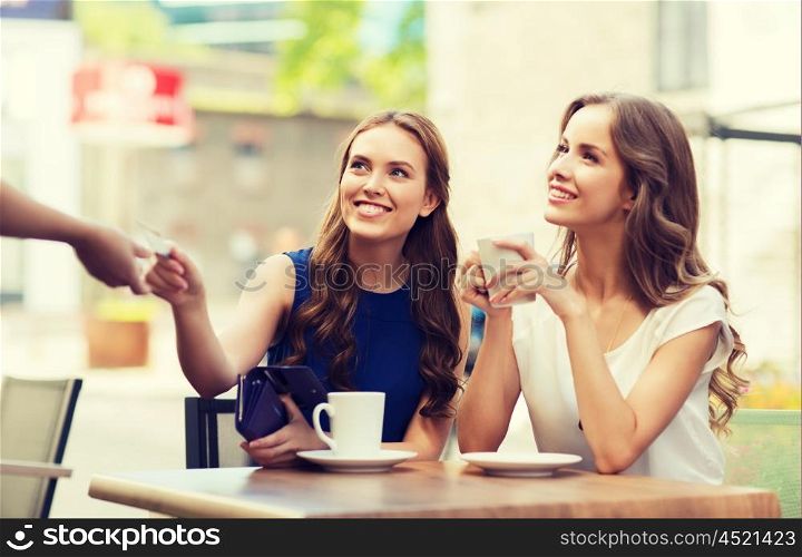 people, consumerism, lifestyle and friendship concept - smiling young women giving credit card to waiter hand and paying for coffee at outdoor cafe