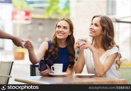 people, consumerism, lifestyle and friendship concept - smiling young women giving credit card to waiter hand and paying for coffee at outdoor cafe