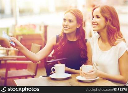 people, consumerism, lifestyle and friendship concept - smiling young women giving money to waiter hand and paying for coffee at outdoor cafe. women paying money to waiter for coffee at cafe