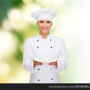 people, cooking and food concept - smiling female chef, cook or baker with empty plate over green background