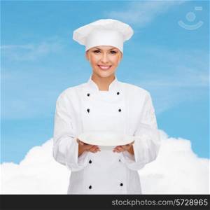 people, cooking and food concept - smiling female chef, cook or baker with empty plate over blue sky with cloud background