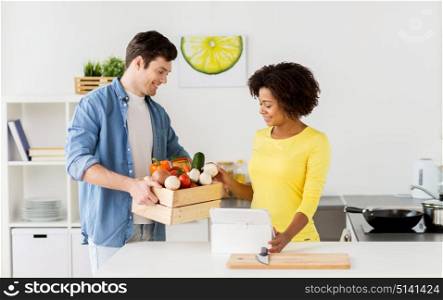 people, cooking and healthy eating concept - happy couple with box of food, vegetables and tablet pc computer at home kitchen. happy couple with healthy food at home kitchen