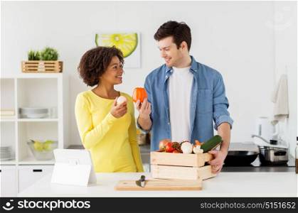people, cooking and healthy eating concept - happy couple with box of food, vegetables and tablet pc computer at home kitchen. happy couple with healthy food at home kitchen