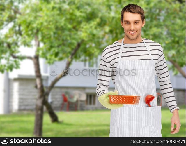people, cooking, culinary and food concept - happy man or cook in apron with baking and kitchenware over summer garden and house background