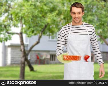 people, cooking, culinary and food concept - happy man or cook in apron with baking and kitchenware over summer garden and house background