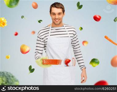 people, cooking, culinary and food concept - happy man or cook in apron with baking and kitchenware over gray background with falling vegetables