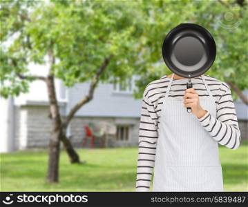 people, cooking, culinary and identity concept - man or cook in apron hiding his face behind frying pan over summer garden and house background